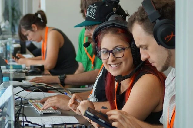 A young woman, seated at a desk among other show producers, smiles for the camera.