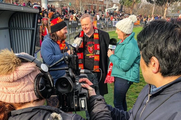 Cameramen watch two interviewers, a man and a woman with microphones, interview Anthony Albanese.
