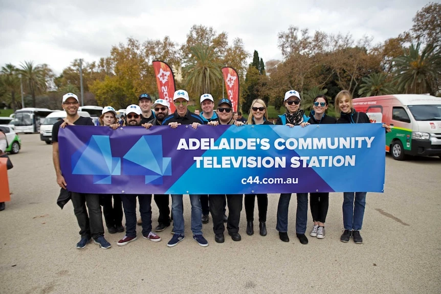12 community television volunteers and staff carry a banner reading 
